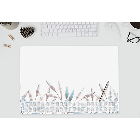 Tapis de bureau avec des feuilles bleu-beige, un clavier, un stylo et des accessoires. Ambiance lumineuse et aérée.