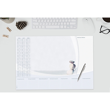 Sous-main blanc avec pierres, stylo, calendrier et notes. En haut à gauche, un pot, des pinces à linge, une pomme de pin et un clavier.