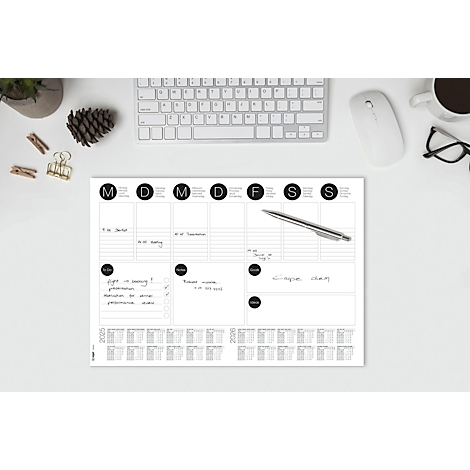 Planificateur hebdomadaire avec des notes manuscrites sur un bureau avec clavier, souris, lunettes et tasse à café. Comprend un stylo à bille.