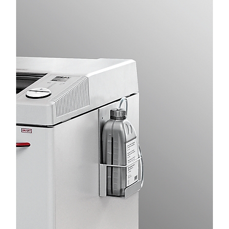 Close-up of a white paper shredder with an attached gray oil bottle in a holder. The bottle has a cap with a hanging loop.