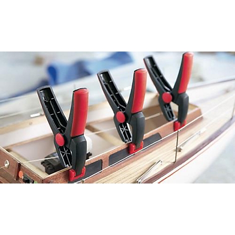Close-up of clamps attached to a model sailboat. The clamps are black with red handles.