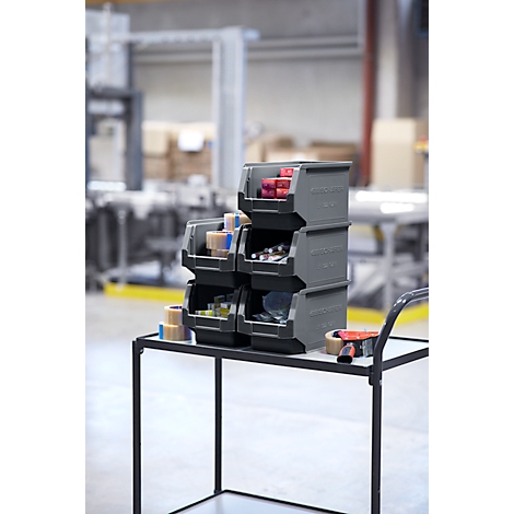 Graue Aufbewahrungsboxen, gefüllt mit Gegenständen, stehen auf einem Rollwagen in einer Fabrikhalle.