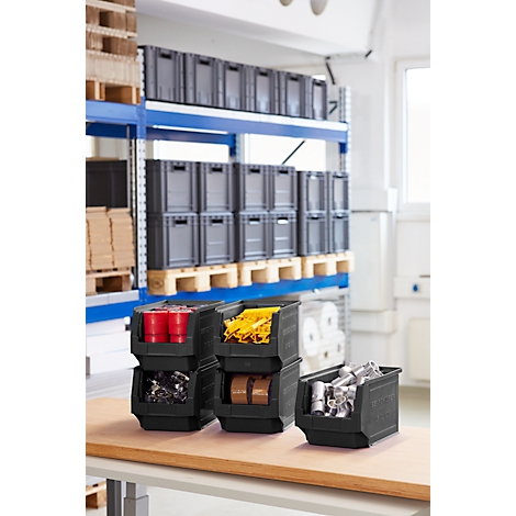 Schwarze Lagerbehälter mit verschiedenen Inhalten, auf einem Tisch platziert. Im Hintergrund ein Regal mit Kisten.