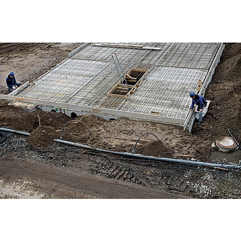 Bouwvakkers die werken aan een betonnen plaat. Staalmatten, aarde en pijpen zijn zichtbaar.