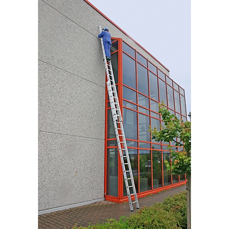 A man in blue overalls climbs a ladder on a building.