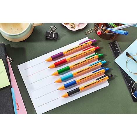 Mehrfarbige Stifte auf kariertem Papier. Auf dem Tisch liegen weitere Büromaterialien.