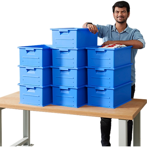 A man stands next to stacked, blue boxes on a table. Some boxes contain clothes.