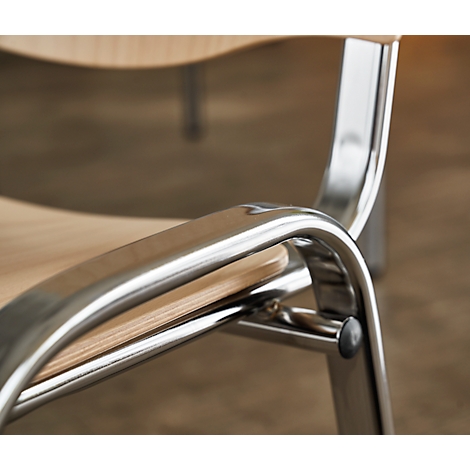 Detail shot of a wooden and metal armchair armrest. The polished metal strut is curved and connects the wooden surface to the chair legs.