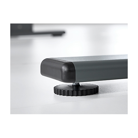 Close-up of a table leg: gray, rectangular with black plastic element, below a black, ribbed adjusting screw.