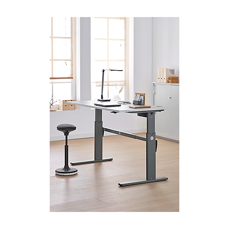 An height-adjustable desk with office chair and lamp against a bright background. The picture shows the product in an office environment.