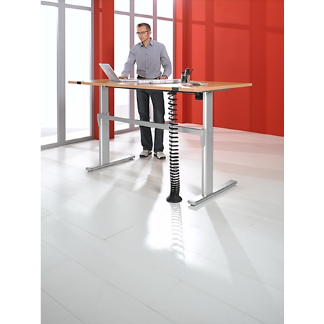A man stands at a height-adjustable desk with a laptop. Red background and white floor.