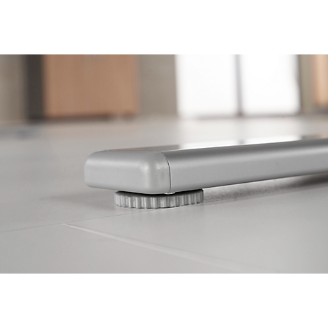 Close-up of a silver table leg construction. The table foot stands on a round, toothed plastic part.