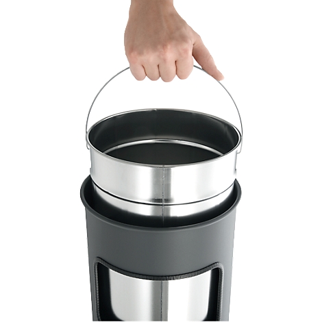 A hand holds a metal bucket, which is inserted into a dark, cylindrical container.