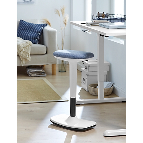 White standing stool, blue seat, in front of a bright desk. In the background: sofa, cushions, home accessories.