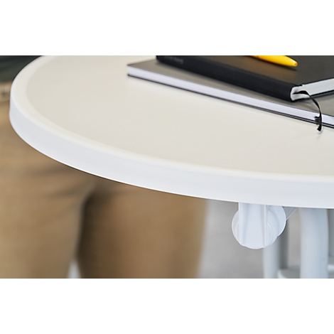 A white table with a rounded edge, on which lies a notebook, behind it a person. The table leg is visible.