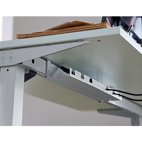 Close-up of a desk showing cable management system. Gray desk top with bracket, below a cable tray.