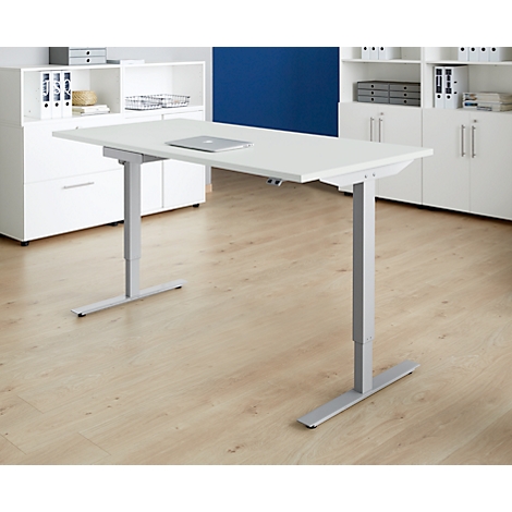 A white, height-adjustable desk with a laptop, set against a background of wooden flooring, white cabinets, and a blue wall.