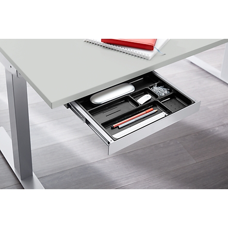 Close-up of a desk drawer with pens, mouse, paper clips. Desk top, grey, metallic legs.