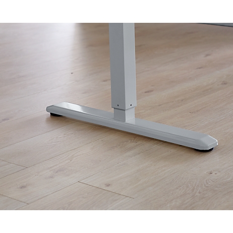 Close-up: Light gray desk foot with black rubber buffer on light wood floor.
