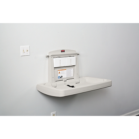 Table à langer murale gris clair, ouverte avec ceinture de sécurité, notice d'information. Prise électrique à gauche.