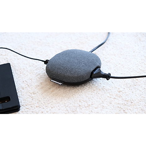 Chargeur rond gris avec étui en tissu sur tapis clair. Câble noir et étui de téléphone à côté.