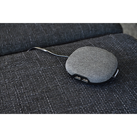 Chargeur ovale gris avec ports USB posé sur un tissu gris foncé.
