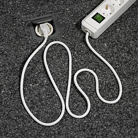 Eine weisse Steckdosenleiste mit einem eingelassenen Stecker in einem grauen Teppichboden, Kabel verläuft geschwungen.