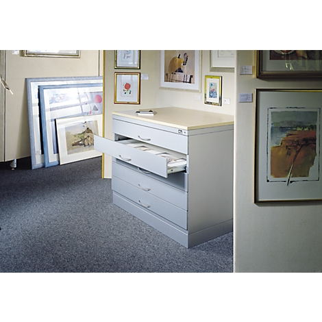 Gray drawer cabinet, one drawer open. Artwork on walls. Gray carpeted floor.