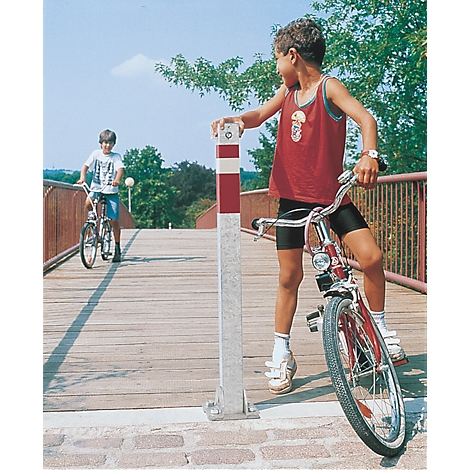 Two boys cycling across a bridge, one holding onto a red and white marker.