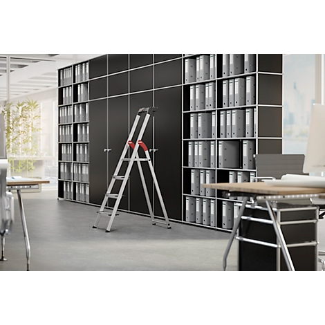 A stepladder stands in front of black file cabinets filled with folders. Office desks are in the background.