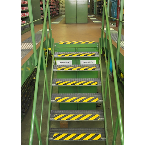 Green metal stairs with yellow and black warning markings in a warehouse. Two signs reading "Lagerstätte." Shelves in the background.