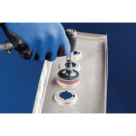 Een gehandschoende hand bedient een gereedschap op een zilveren metalen plaat met ronde onderdelen.