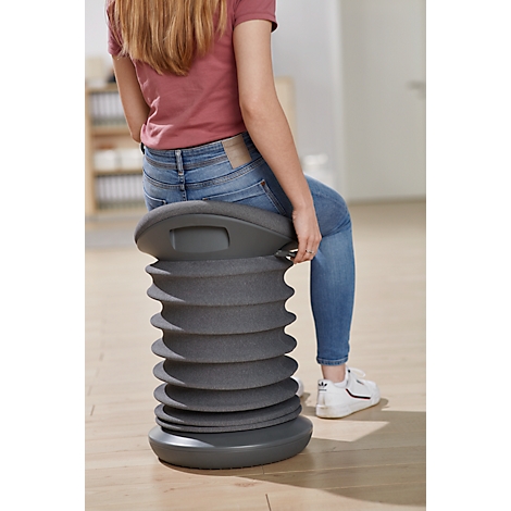 A girl sits on a gray, spiral-shaped stool. She is wearing jeans and a red t-shirt.