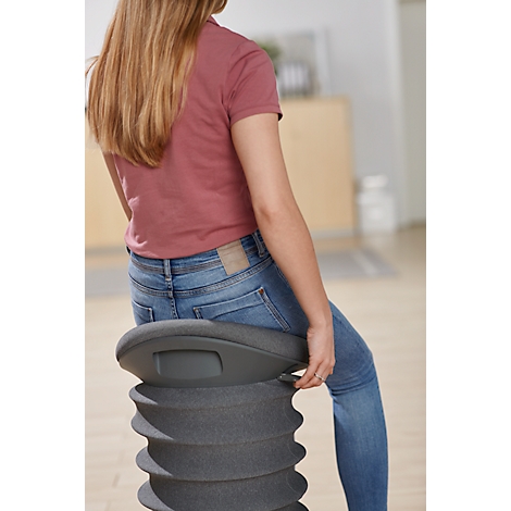 Young woman sitting on a grey, spiral-shaped stool, wearing jeans and a red shirt. The background is blurred.