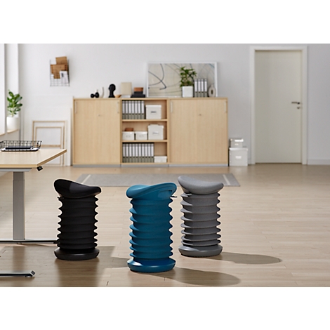 Three height-adjustable stools in black, blue and grey in front of an office background.