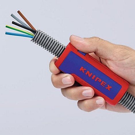 Hand holding a red, blue KNIPEX tool. Cables are in a gray corrugated tube. Some wires are sticking out.