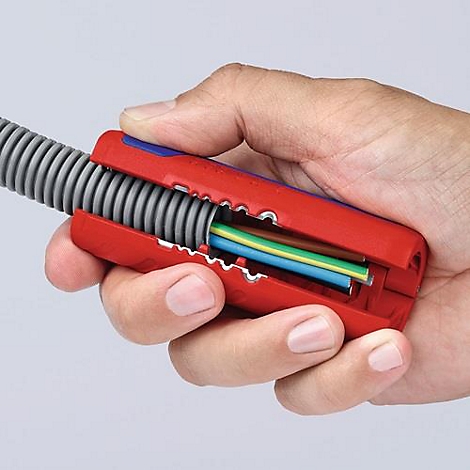 Hand holding a cable stripping tool. Red pliers, gray tube, colored cables visible.