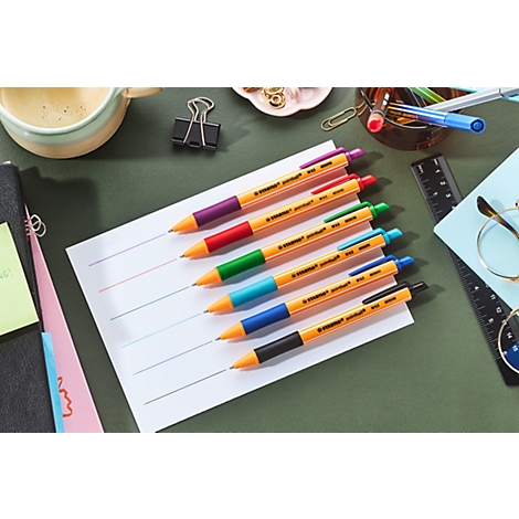 Des stylos colorés sur papier, entourés de fournitures de bureau.
