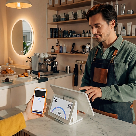 Ein Kunde bezahlt kontaktlos mit dem Smartphone an einem Kassenterminal in einem Café.