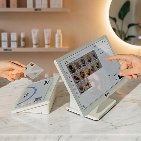 Ein Kassenterminal mit Touchscreen auf einem Marmortresen, während eine Karte kontaktlos an ein Lesegerät gehalten wird.