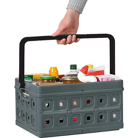 Person hält graue, zusammenklappbare Einkaufskiste mit Produkten. Schwarzer Griff. Kiste ist gefüllt mit Lebensmitteln, wie Senf, Marmelade und Öl.