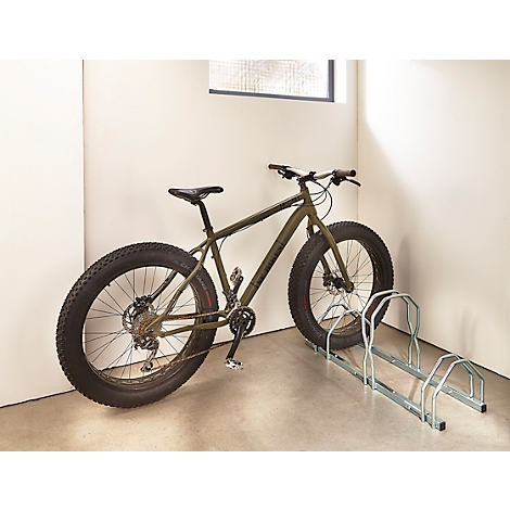 Un fatbike vert olive est à côté d'un porte-vélos dans un coin clair.