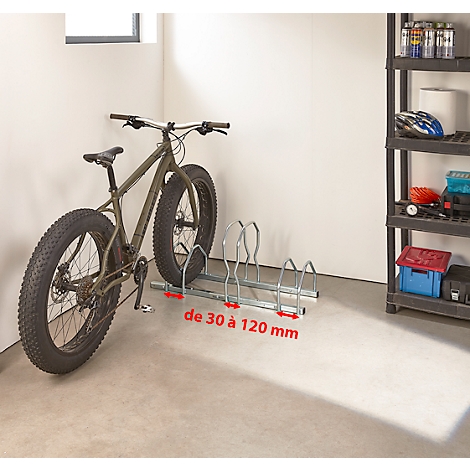 Un vélo fatbike vert est dans un porte-vélos avec l'inscription "de 30 à 120 mm". Des ustensiles sont sur une étagère à côté.