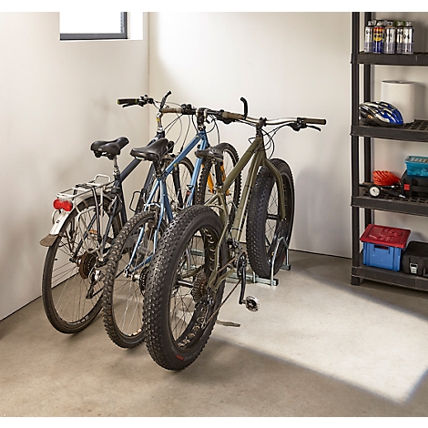 Trois vélos sont dans un garage. L'un est un fat bike, les autres sont des vélos normaux. A droite, une étagère avec des accessoires.