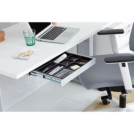 Bureau blanc avec un tiroir ouvert rempli de fournitures de bureau. À côté, une chaise de bureau.
