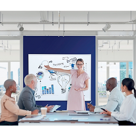 Une femme présente des graphiques à une équipe dans une salle de réunion. Elle pointe vers un tableau de présentation tandis que l'équipe regarde attentivement.