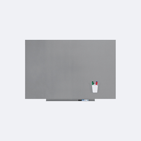 Tableau magnétique gris avec porte-stylos et stylos. Une étagère en dessous, à côté des stylos. Ambiance lumineuse.