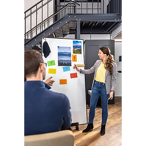 Une femme fait une présentation devant un tableau blanc avec des notes tandis qu'un collègue l'écoute attentivement.