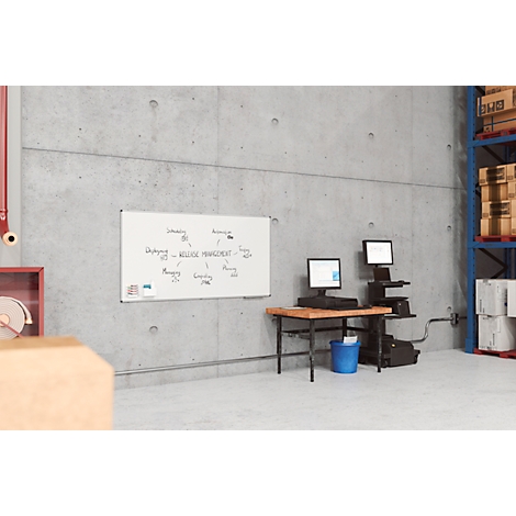 Un espace d'entrepôt, avec un bureau et des ordinateurs. Au mur, un tableau blanc avec des notes.