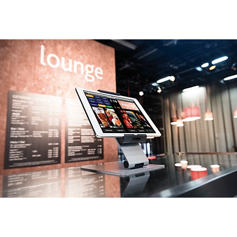 A tablet on a table displays menus. In the background, a sign reads "lounge."